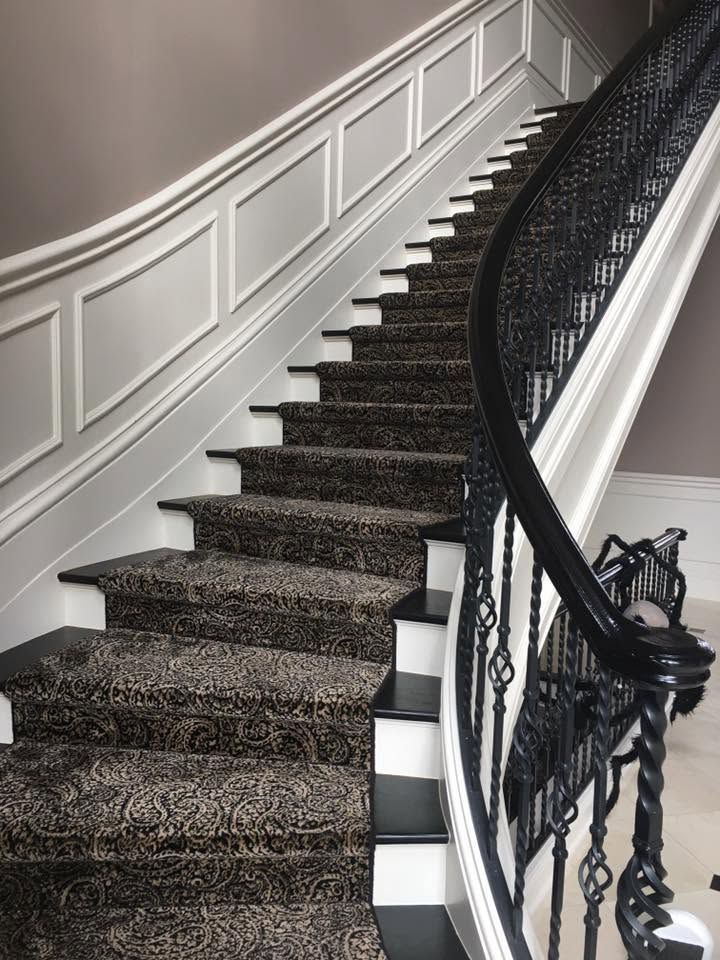 Curved carpeted staircase with white paneled wall and ornate black railing