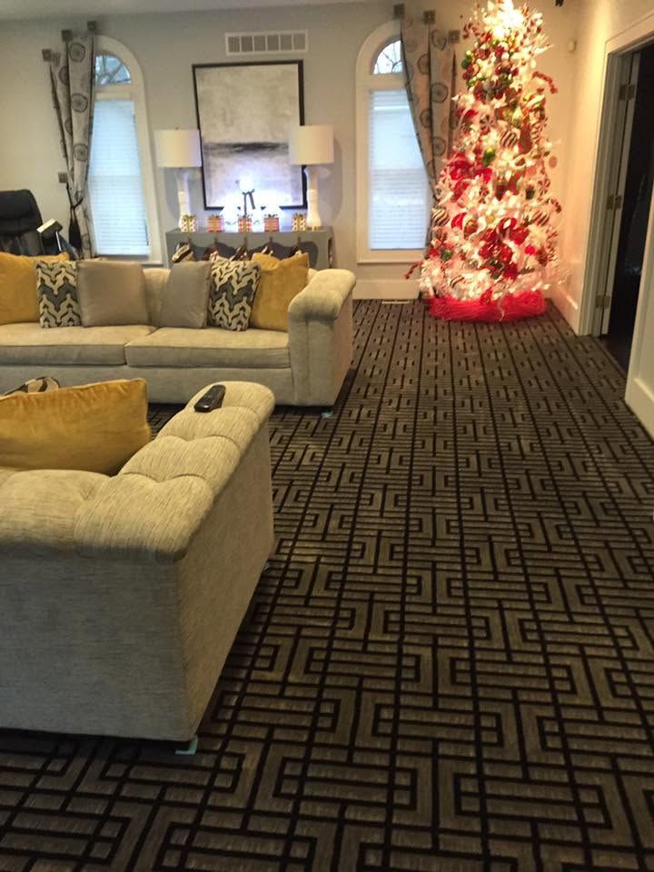Living room with beige sofas, patterned carpet, and a decorated Christmas tree by the wall.
