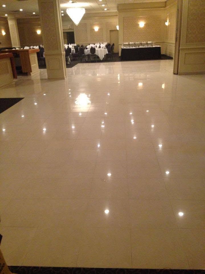 Empty ballroom with glossy tiled floor and chandeliers, banquet tables at the far end.