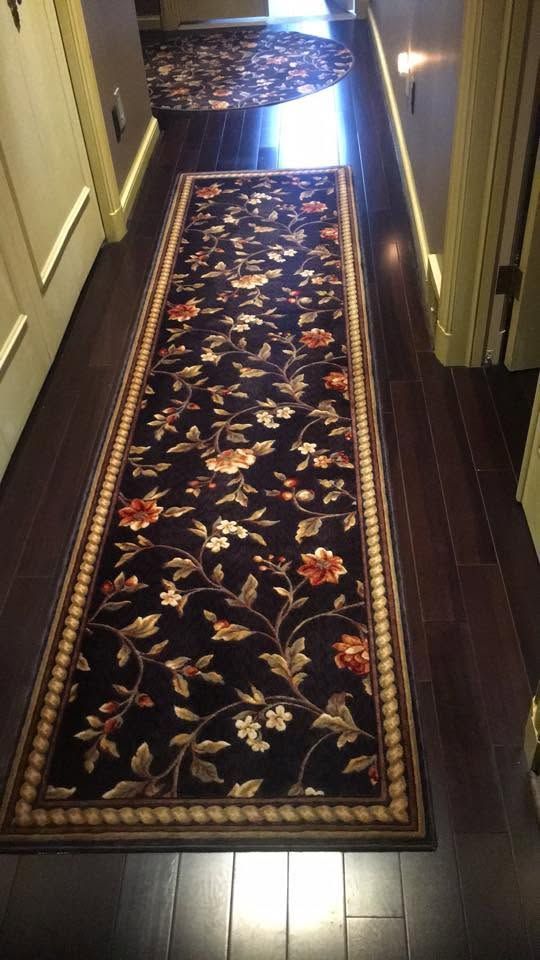 Narrow hallway with dark wood floors and a long floral runner rug leading to a bright doorway.