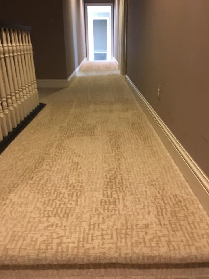 Carpeted hallway with beige walls and a doorway at the far end, lit by soft natural light
