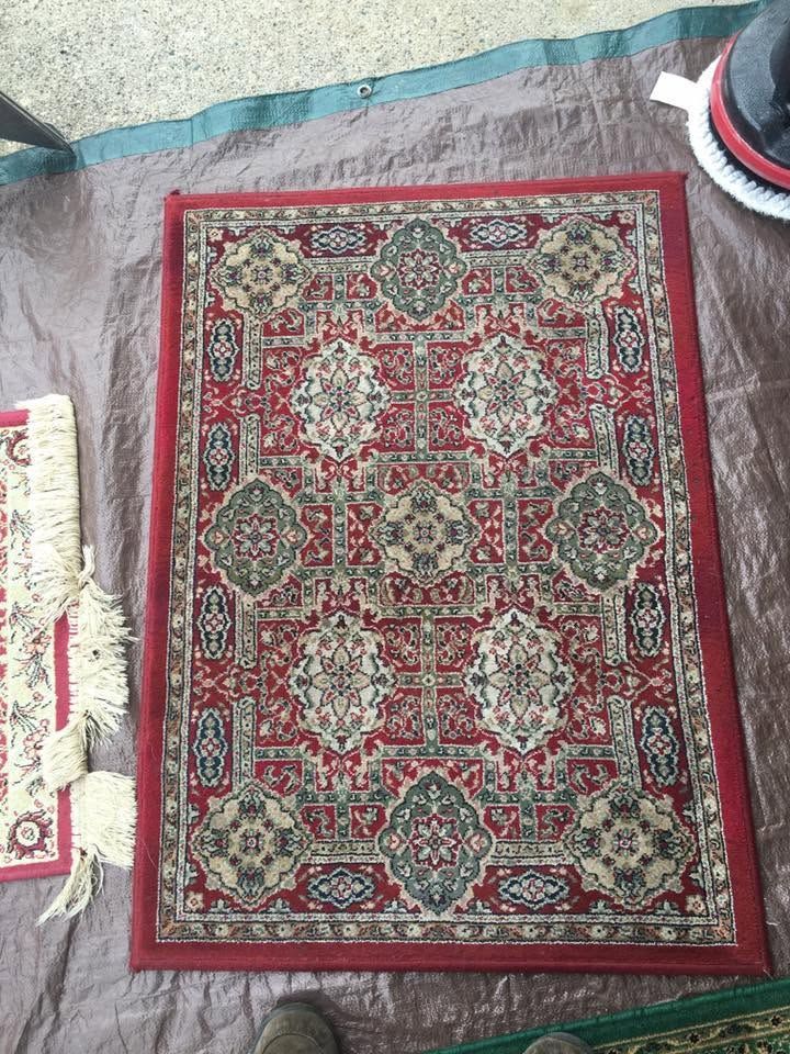 Red patterned prayer rug on a carpeted floor, with a shoe visible at the top right.