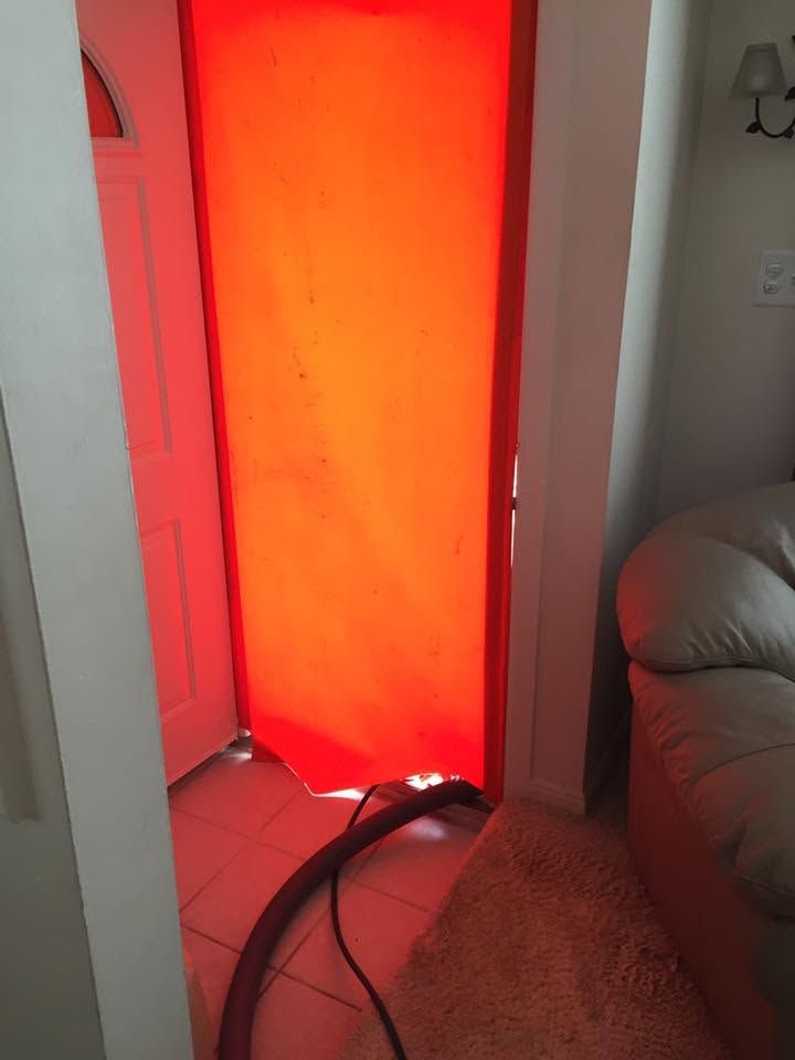 Red glowing panel in a doorway with cords on the floor beside a couch and carpet.