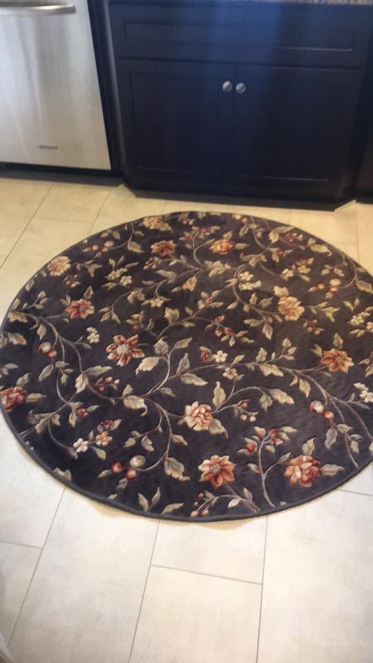 Round floral rug on light tile kitchen floor beside dark cabinets and stainless appliance.