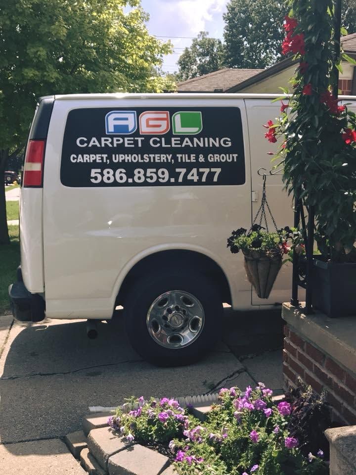 White A.G.L Carpet Cleaning van parked beside a brick planter with flowers