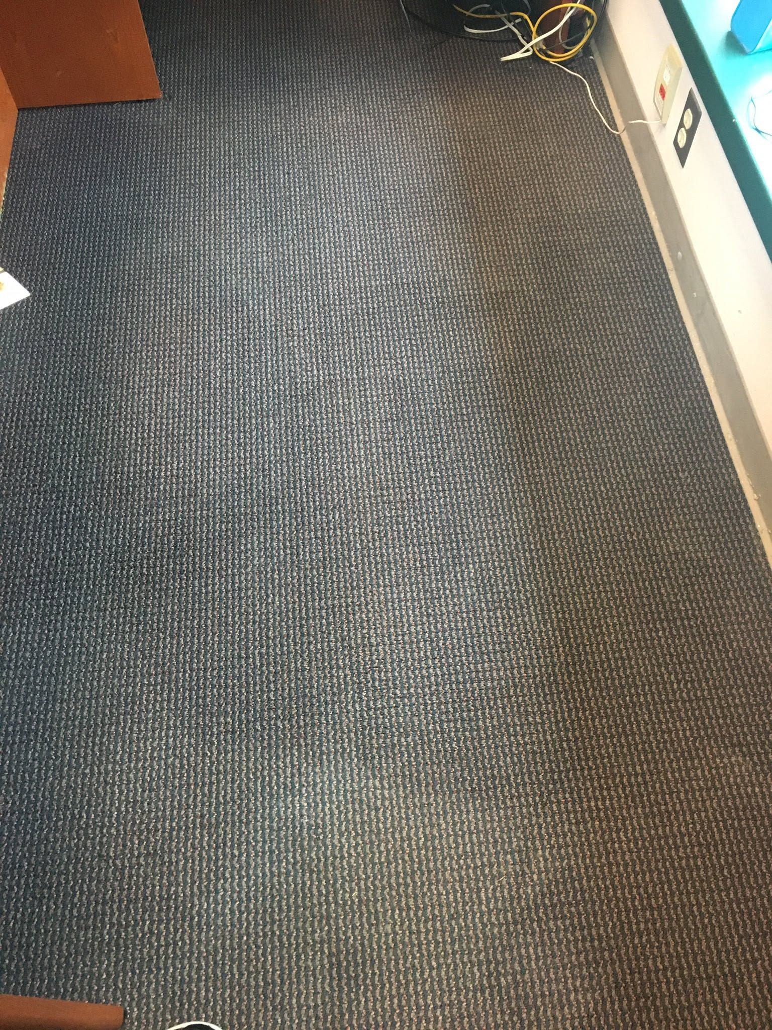 Close-up of a gray textured carpet with a few cables near the top edge