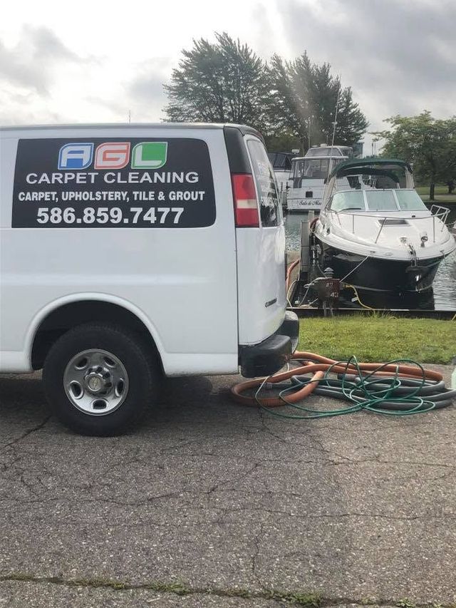 White carpet cleaning van with logo and phone number parked beside a boat trailer in a lot