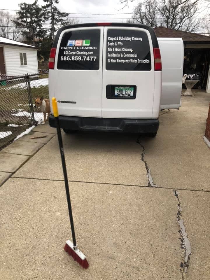 White work van parked in a driveway with a long-handled squeegee or broom leaning against the wet pavement.