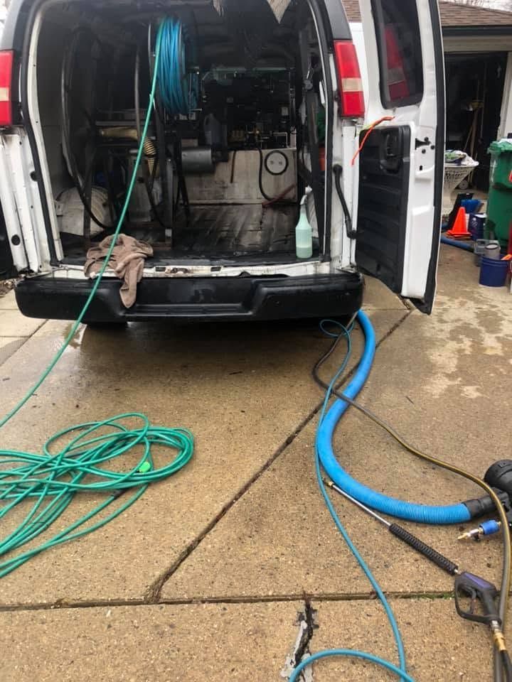 Open van parked in a wet driveway with hoses and cleaning equipment inside and on the ground