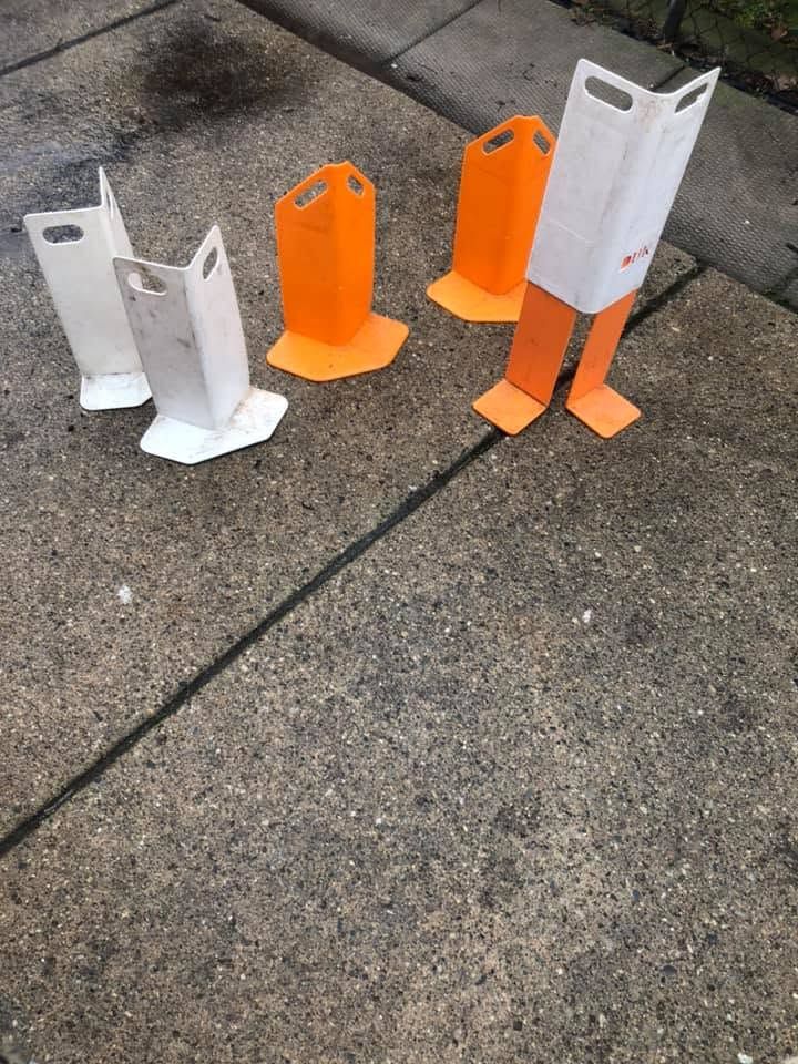 Small white and orange plastic safety posts standing on a concrete sidewalk and curb.