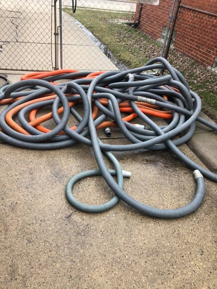 Coiled gray and orange hoses piled on a concrete path beside a chain-link fence and brick wall