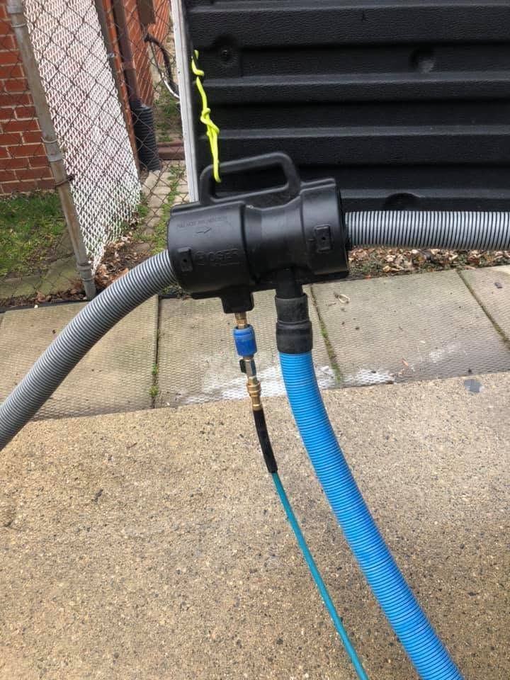 Black pipe connector joining gray, blue, and ribbed hoses on a wet sidewalk by brick stairs