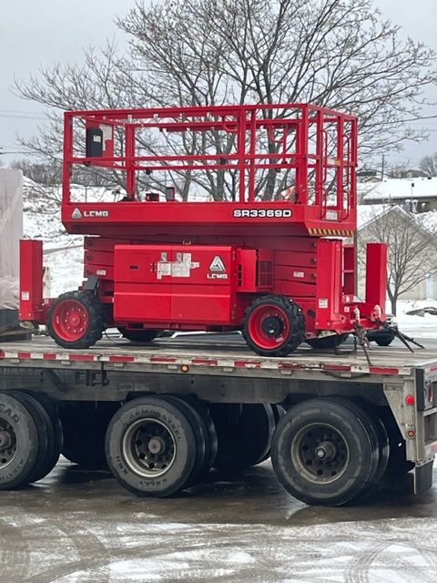 Red scissor lift on a flatbed trailer, in an outdoor setting.