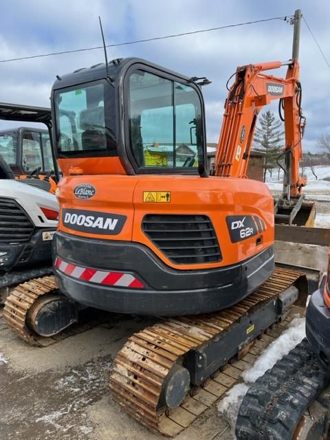 Orange Doosan DX60R excavator parked outside on a cloudy day.