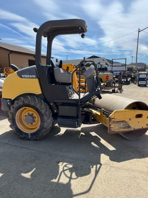 Yellow and black Volvo asphalt compactor on asphalt. Outdoors, sunny day.