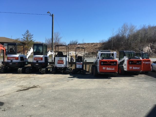 Several Bobcat construction vehicles parked outdoors on a sunny day.