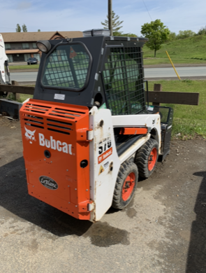 Bobcat S17 skid-steer loader, orange and white, parked on pavement, with safety cage.