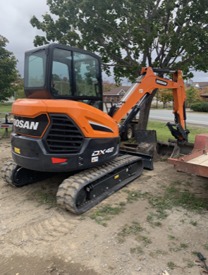 Orange and black Doosan DX42 mini excavator on a construction site, near a small hole.