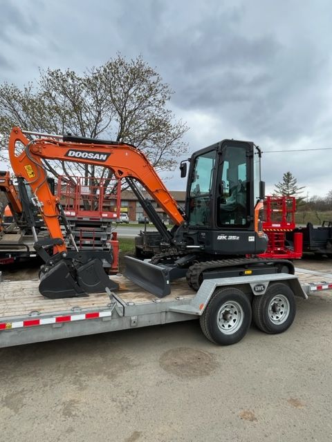 Orange and black Doosan mini excavator on a trailer, under a cloudy sky.