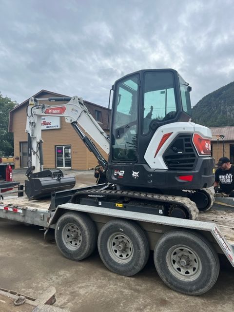 Bobcat E32 compact excavator on a trailer, parked outdoors under cloudy skies.