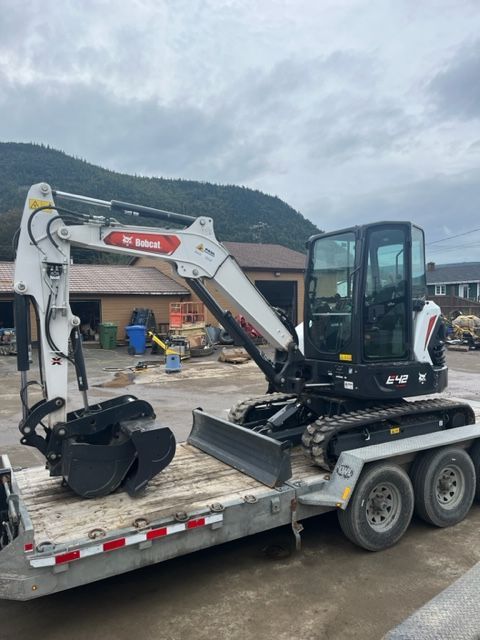 Bobcat excavator on a trailer, ready for transport. White, black, and red details. Cloudy sky.