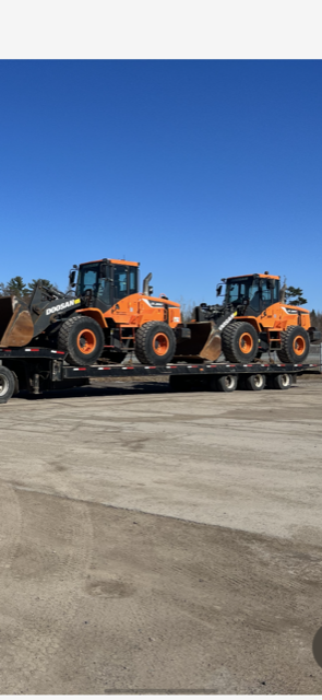 Two orange loaders on a flatbed trailer under a blue sky.