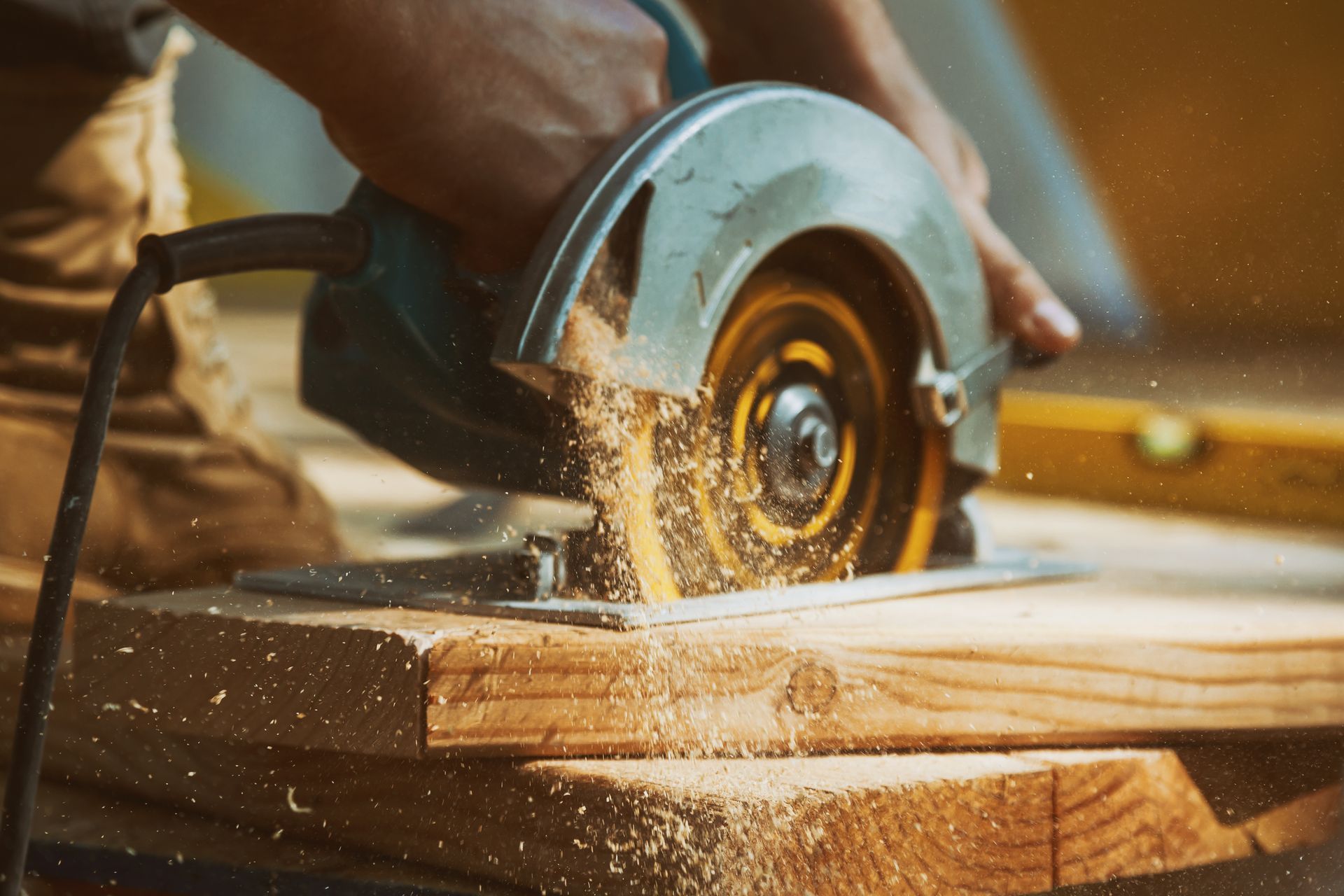Person using a circular saw to cut a wooden board, sawdust in the air.