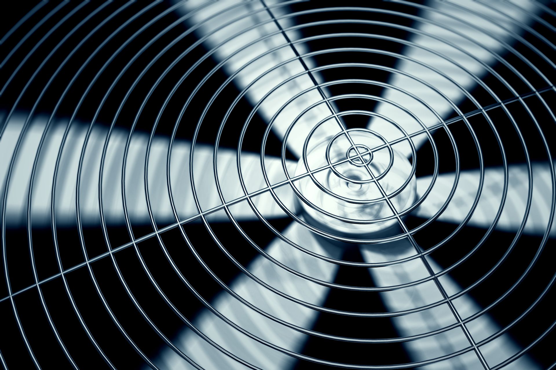 Close-up of a metal fan with a protective grill, blades blurred from motion, cool blue tones.