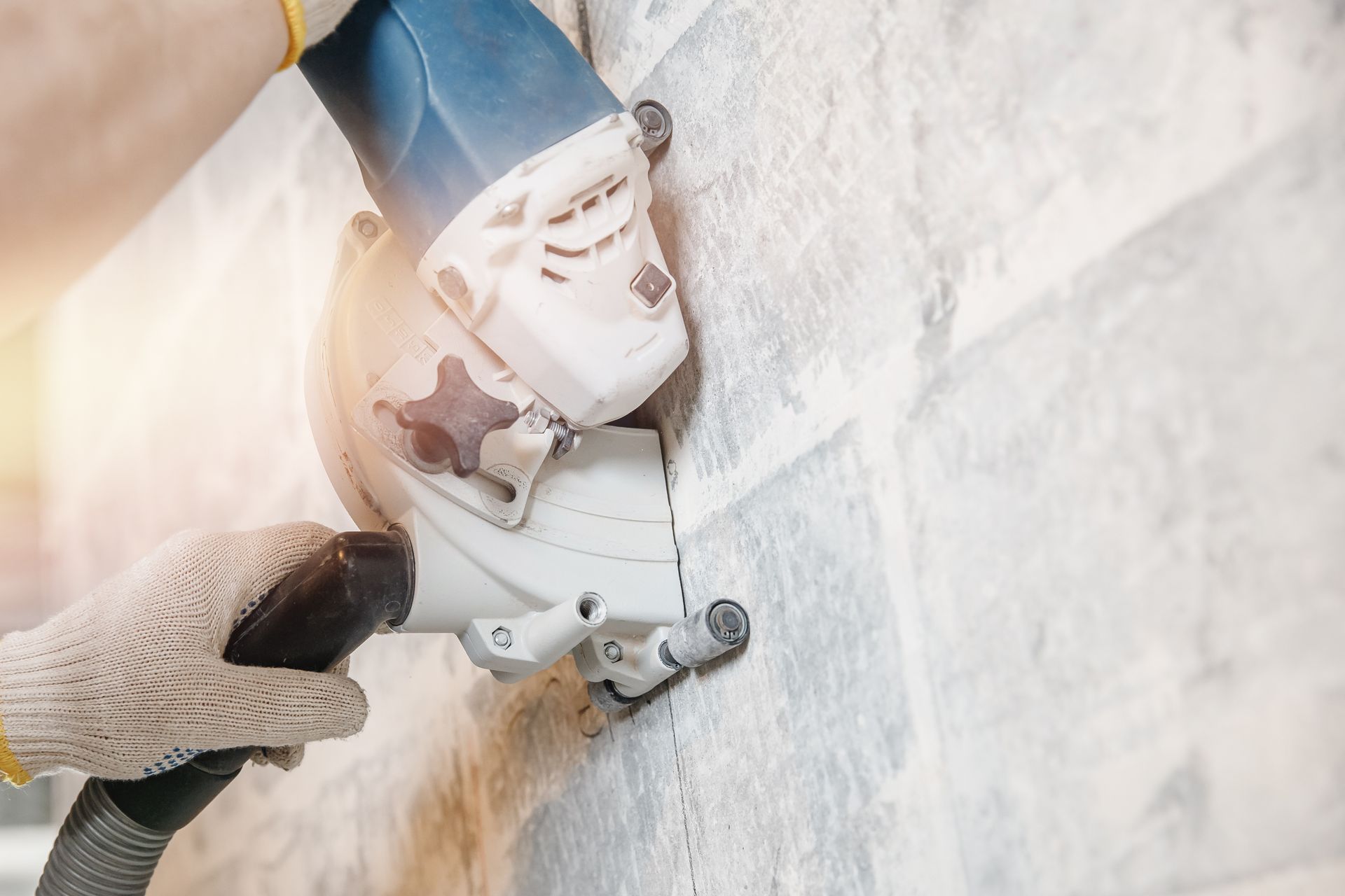 Person using a wall saw to cut into a light-colored wall, with dust collection hose attached.