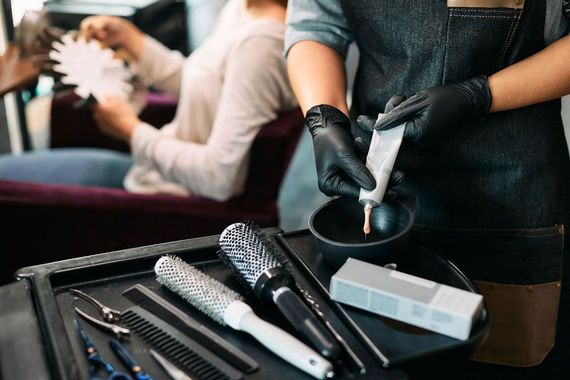 Close-up of hairstylist squeezes hair color from tube while working in salon