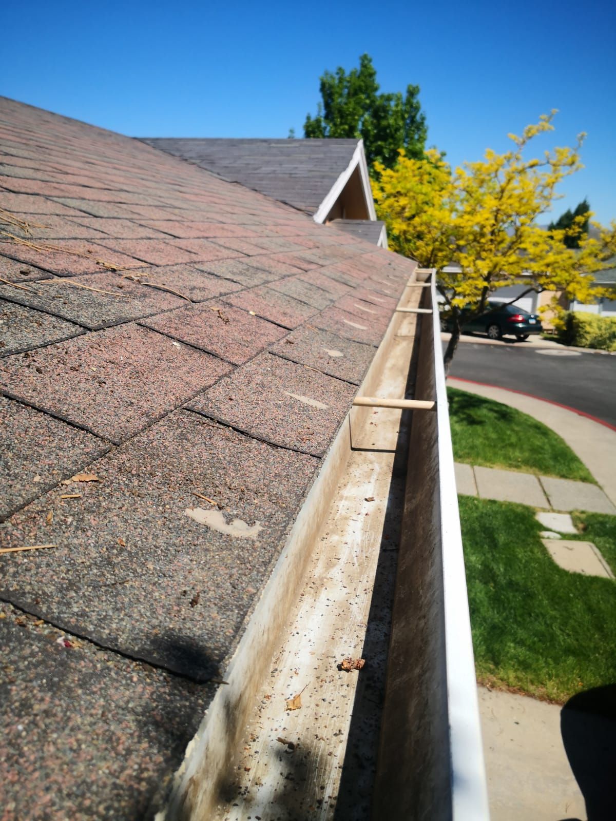 A view looking down the length of a roof gutter, showing shingles on the left and a residential street in the background.