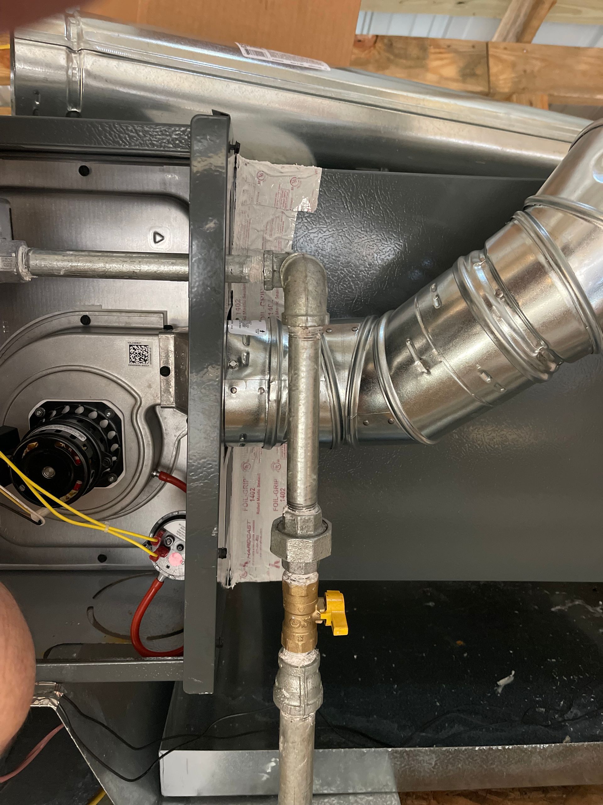 Close-up of HVAC ductwork with a metal connector, insulated pipe, and wiring inside an equipment cabinet