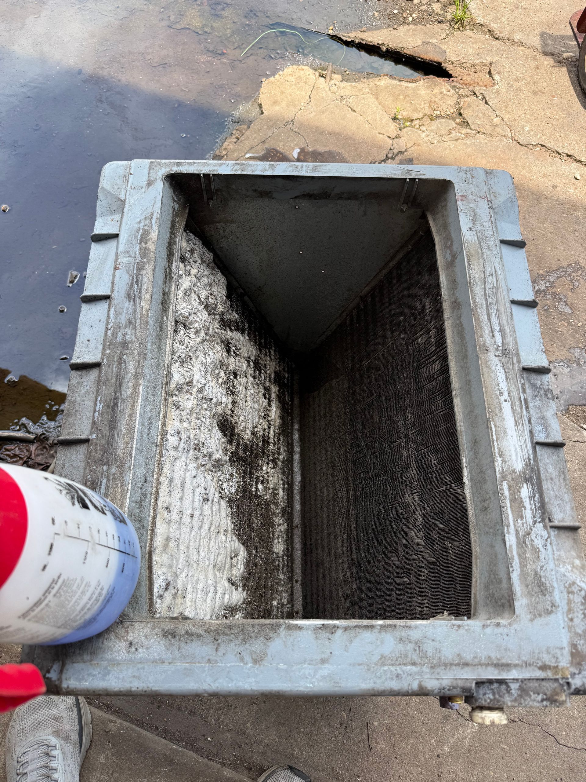 Open rectangular drainage pit with gray concrete frame and sandy water nearby