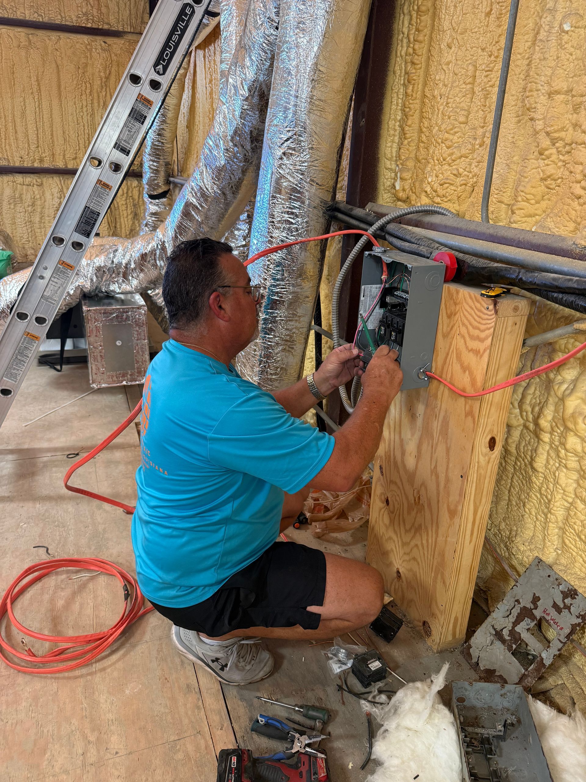 Worker installing wiring in a wall cavity with spray foam insulation, using tools in a construction area.