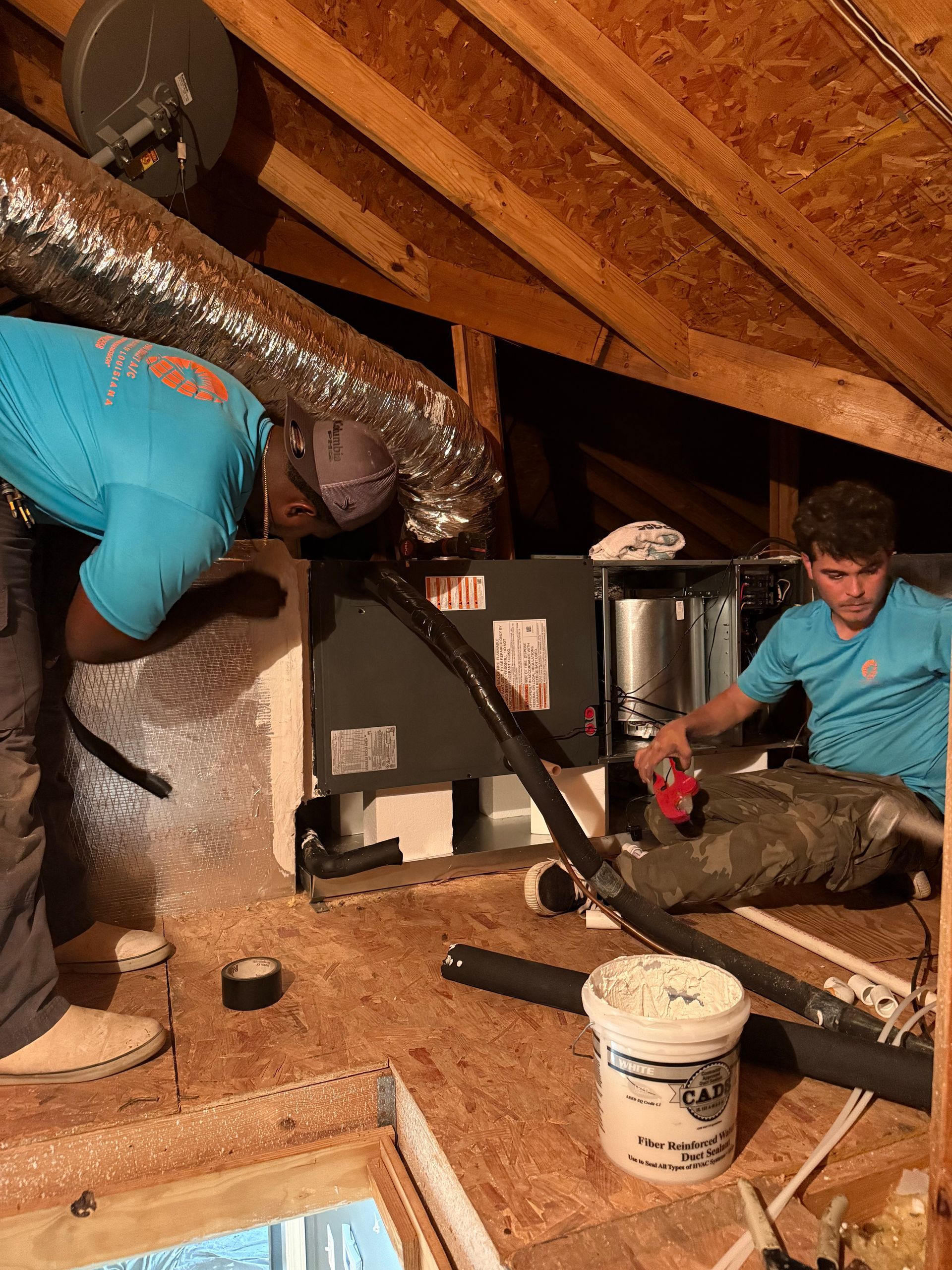 Workers installing HVAC ducting in an attic with exposed beams and insulation.