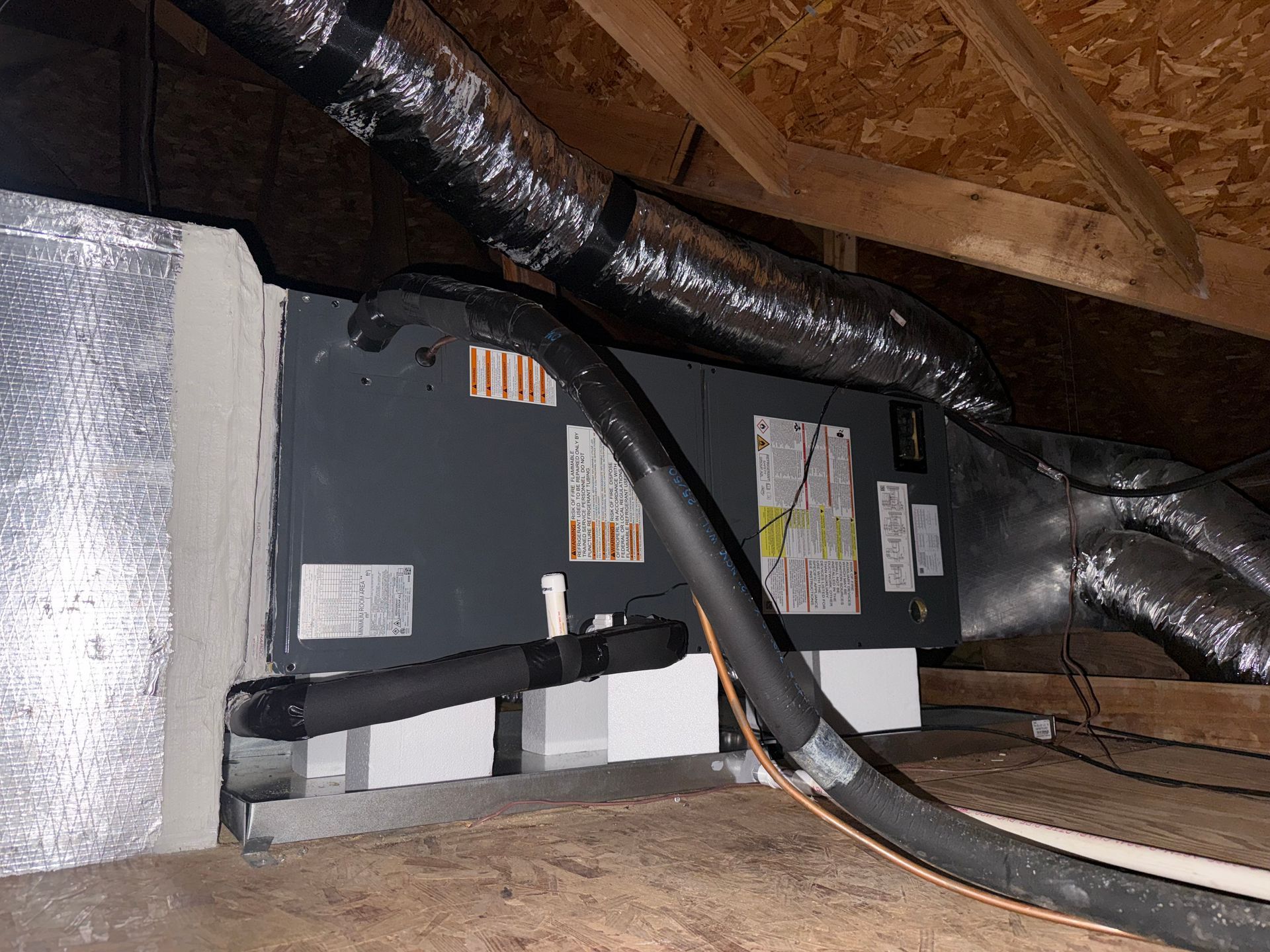 HVAC equipment in an attic with insulated ductwork and black cables beneath roof rafters