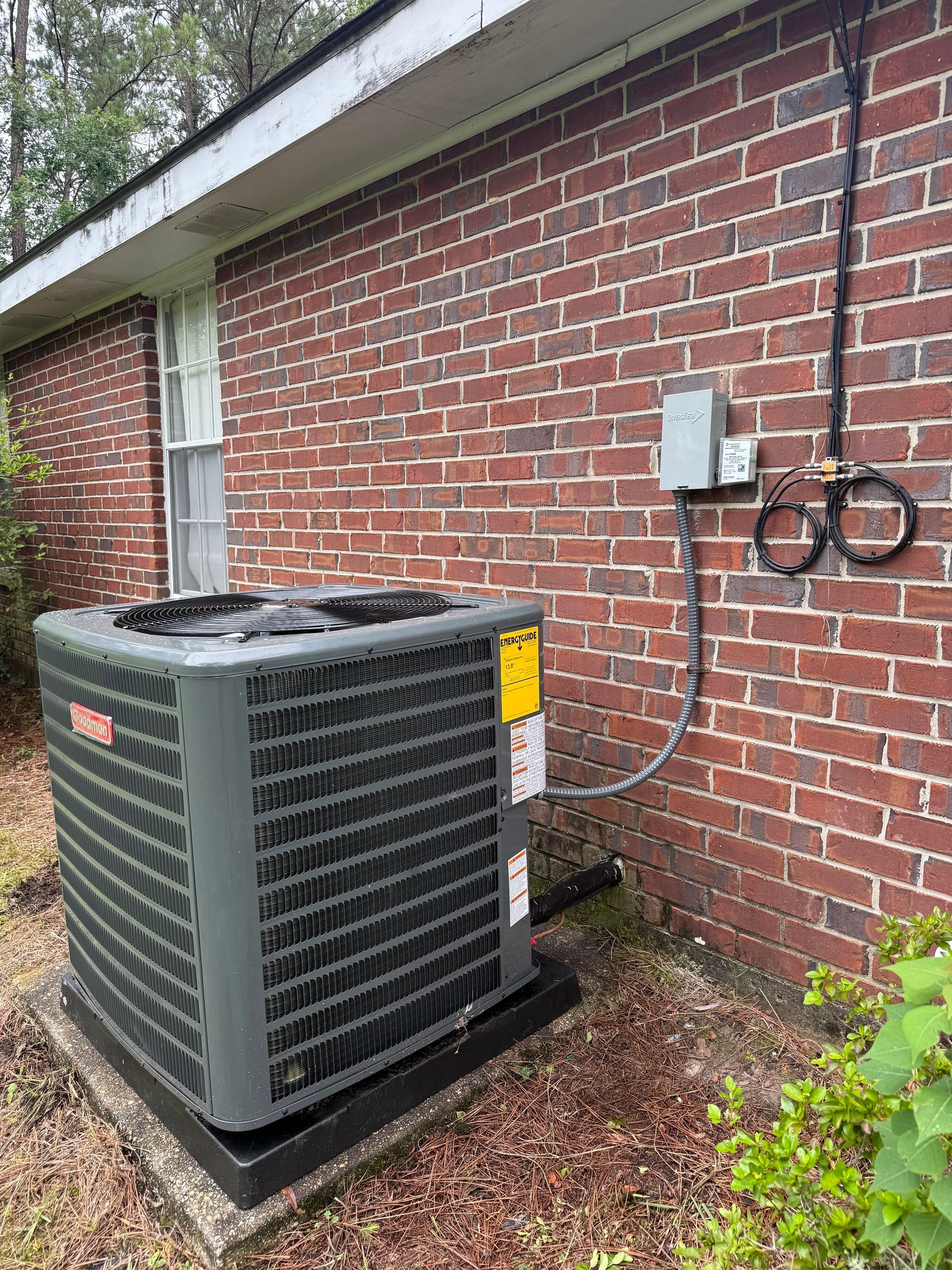 Outdoor air conditioning unit beside a red brick house wall with electrical conduit and utility boxes