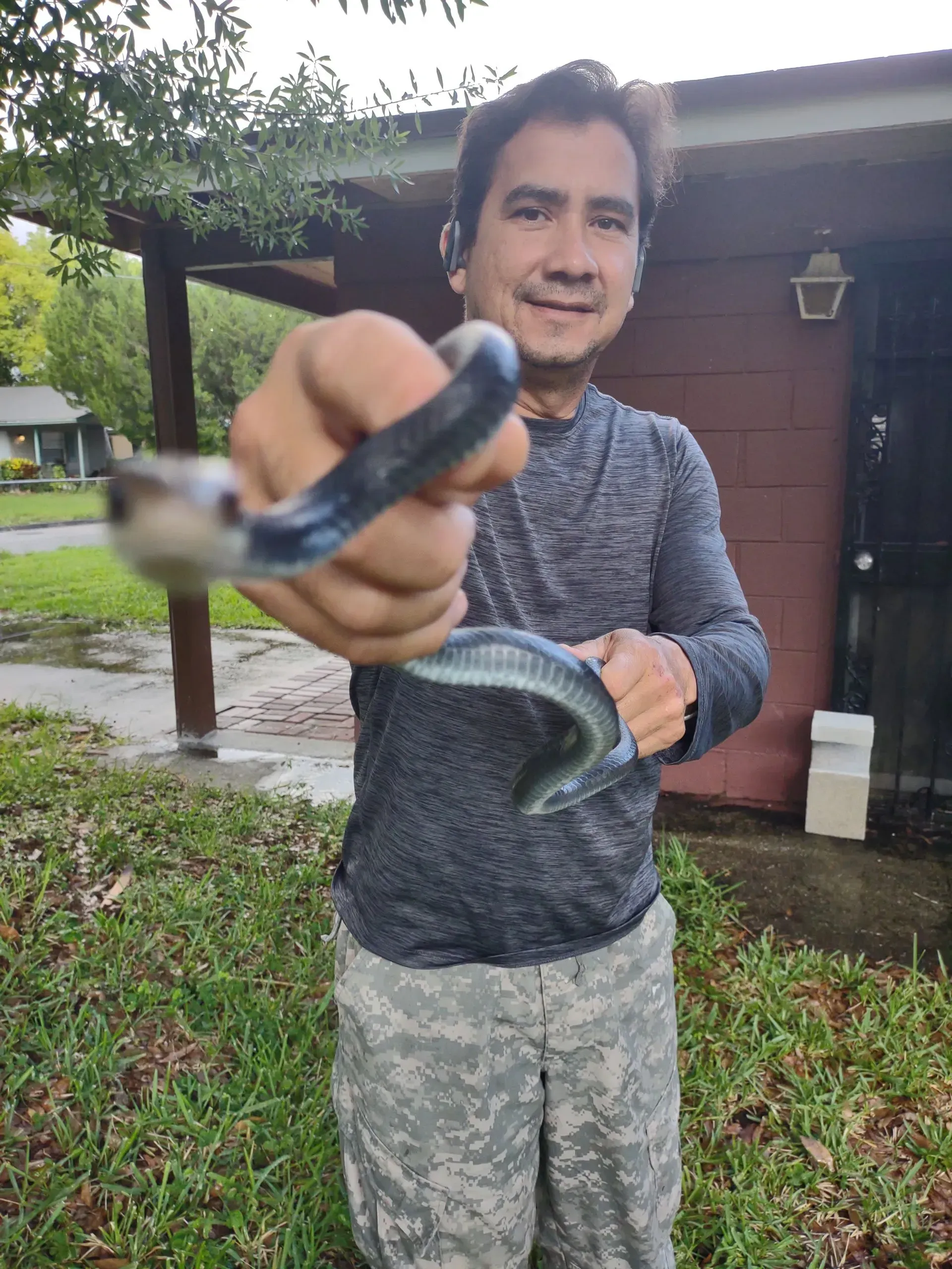 Edgar Nunez holding a snake in front of a house