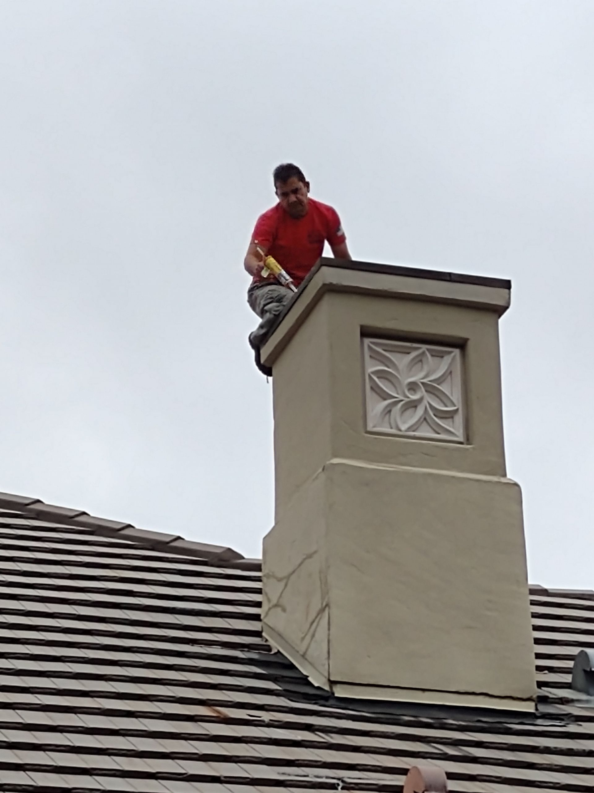 A man is sitting on top of a chimney on a roof