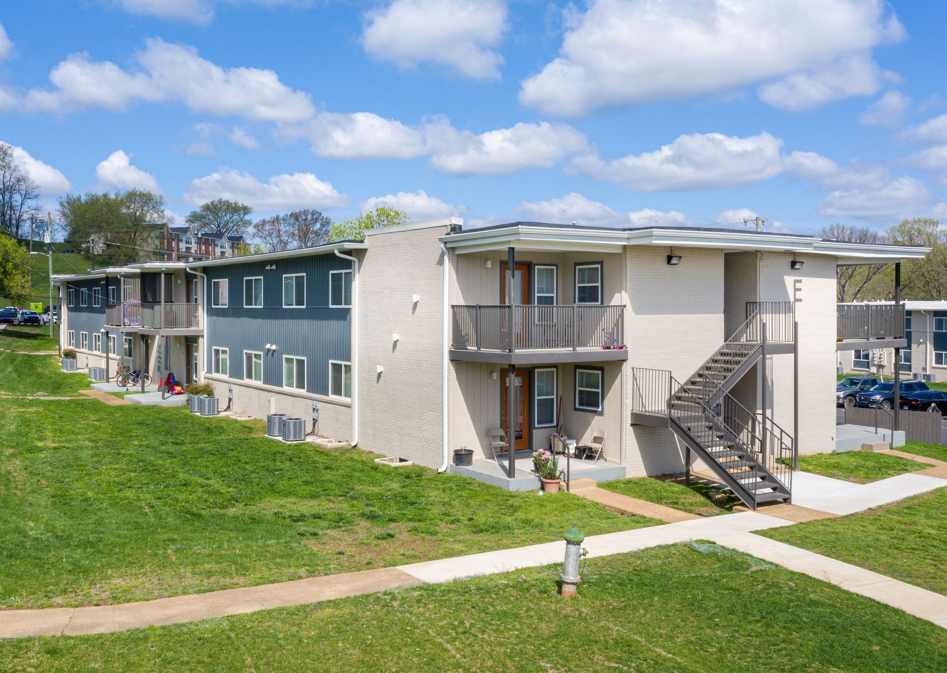 A two-story apartment building with beige brick and dark blue siding, featuring exterior staircases and small balconies.