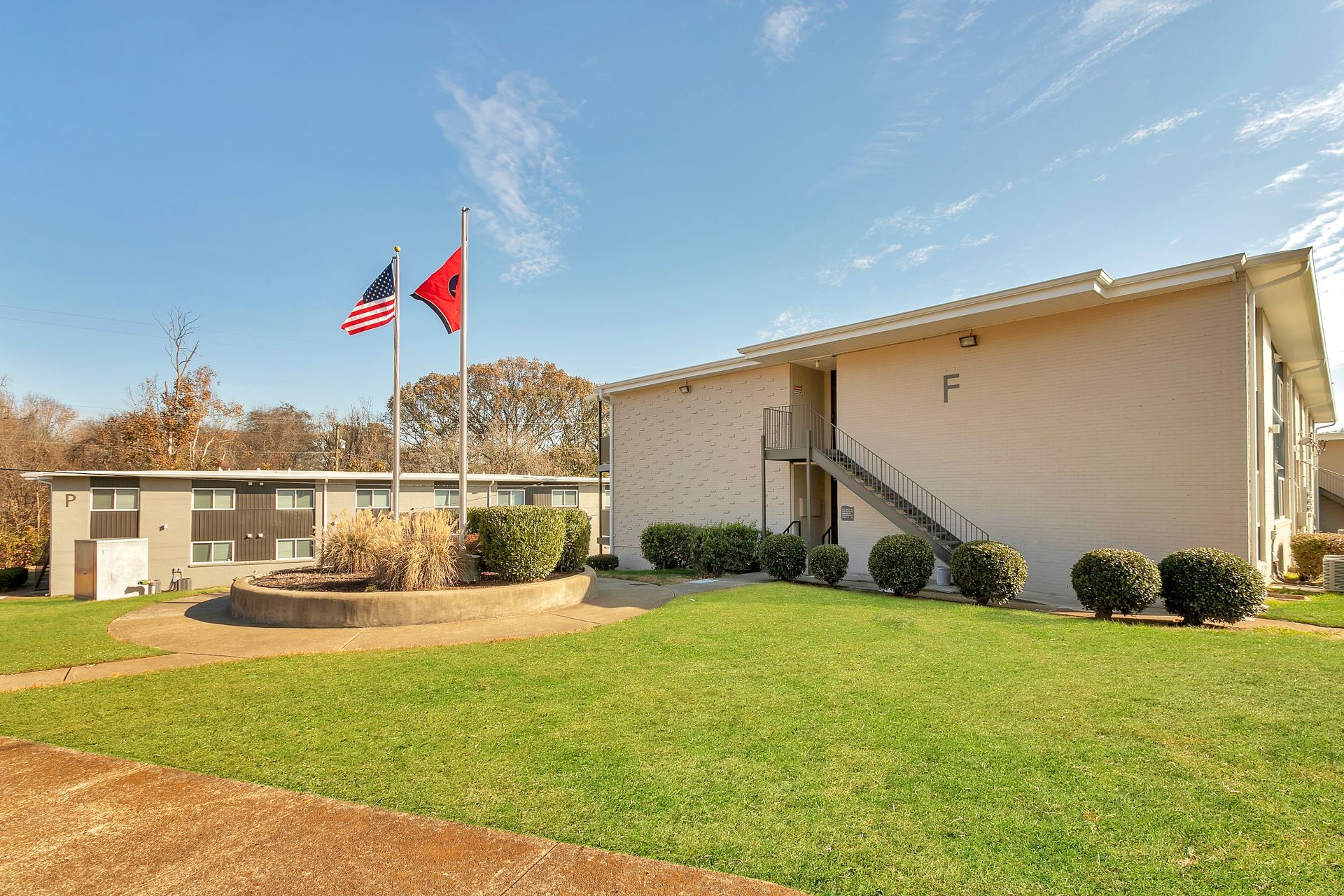 Two-story apartment buildings with light siding under a blue sky, featuring a US flag and an Alabama state flag.