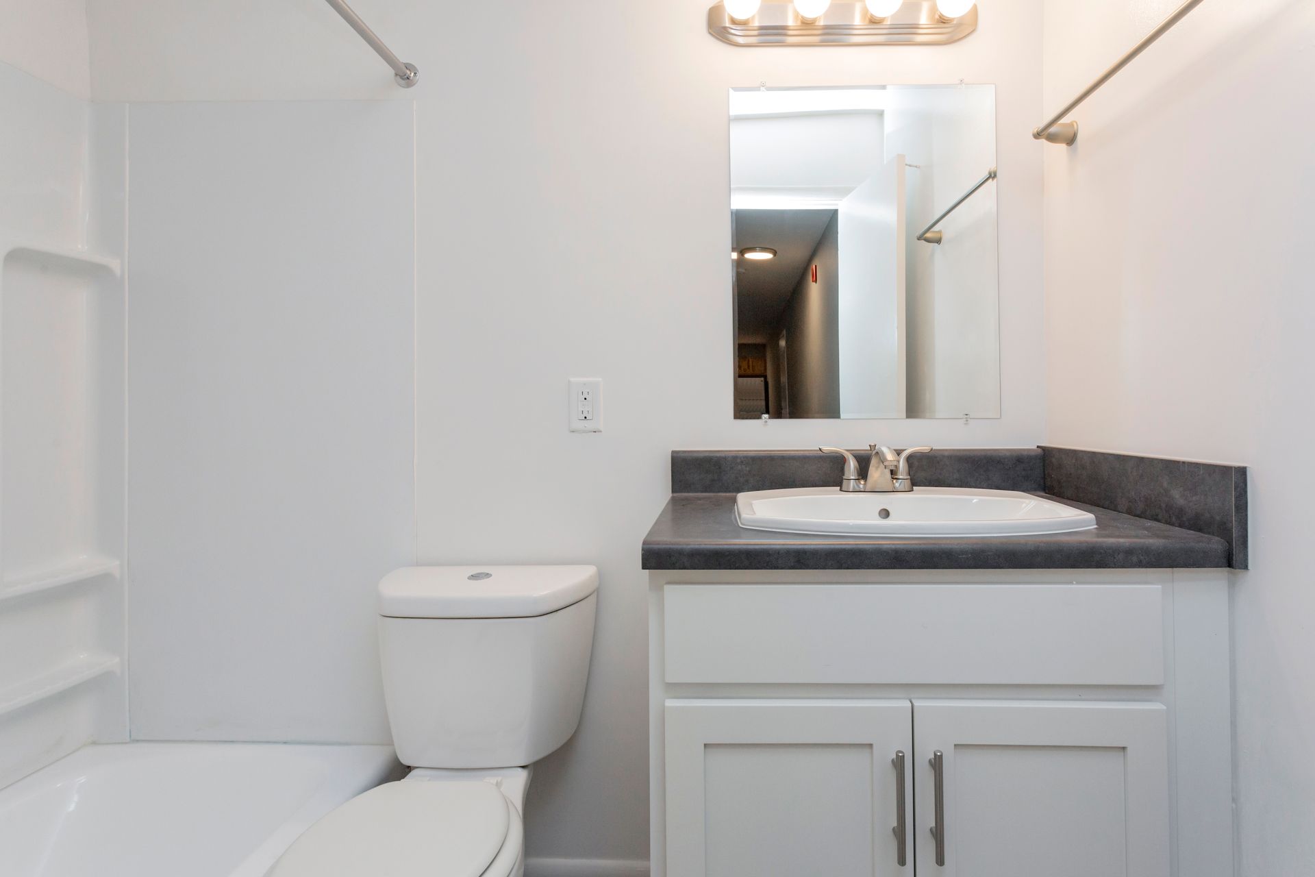 A modern bathroom with a white bathtub, toilet, and vanity with a dark gray countertop and mirror.