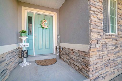 Front porch with turquoise front door, stone siding, and a welcome wreath on the door. Front porch with turquoise front door, stone siding, and a welcome wreath on the door.
