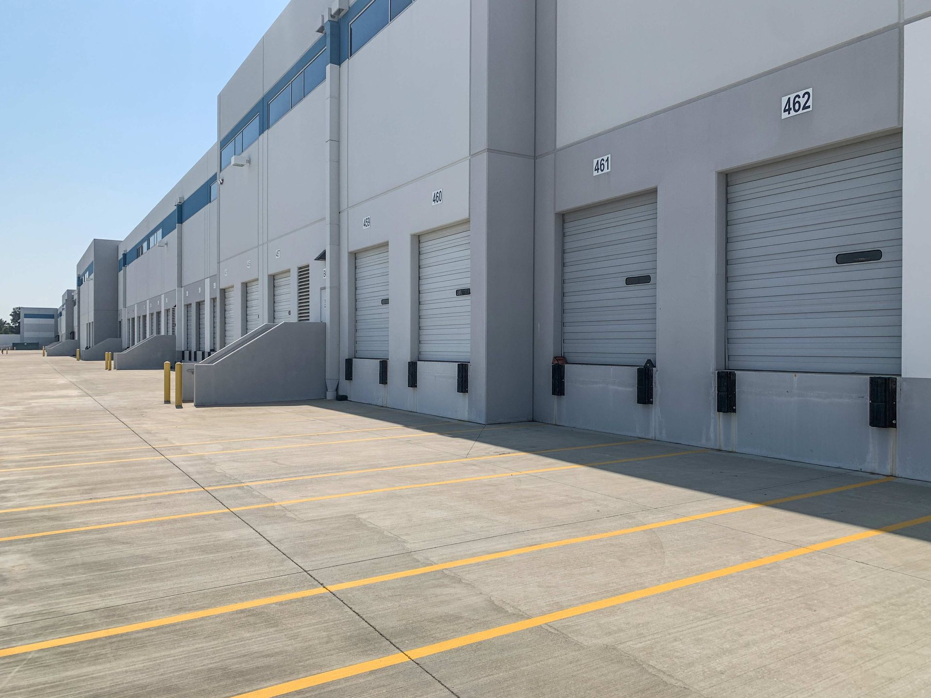 Row of gray warehouse loading docks along a concrete lot with yellow lane markings. Row of gray warehouse loading docks along a concrete lot with yellow lane markings.