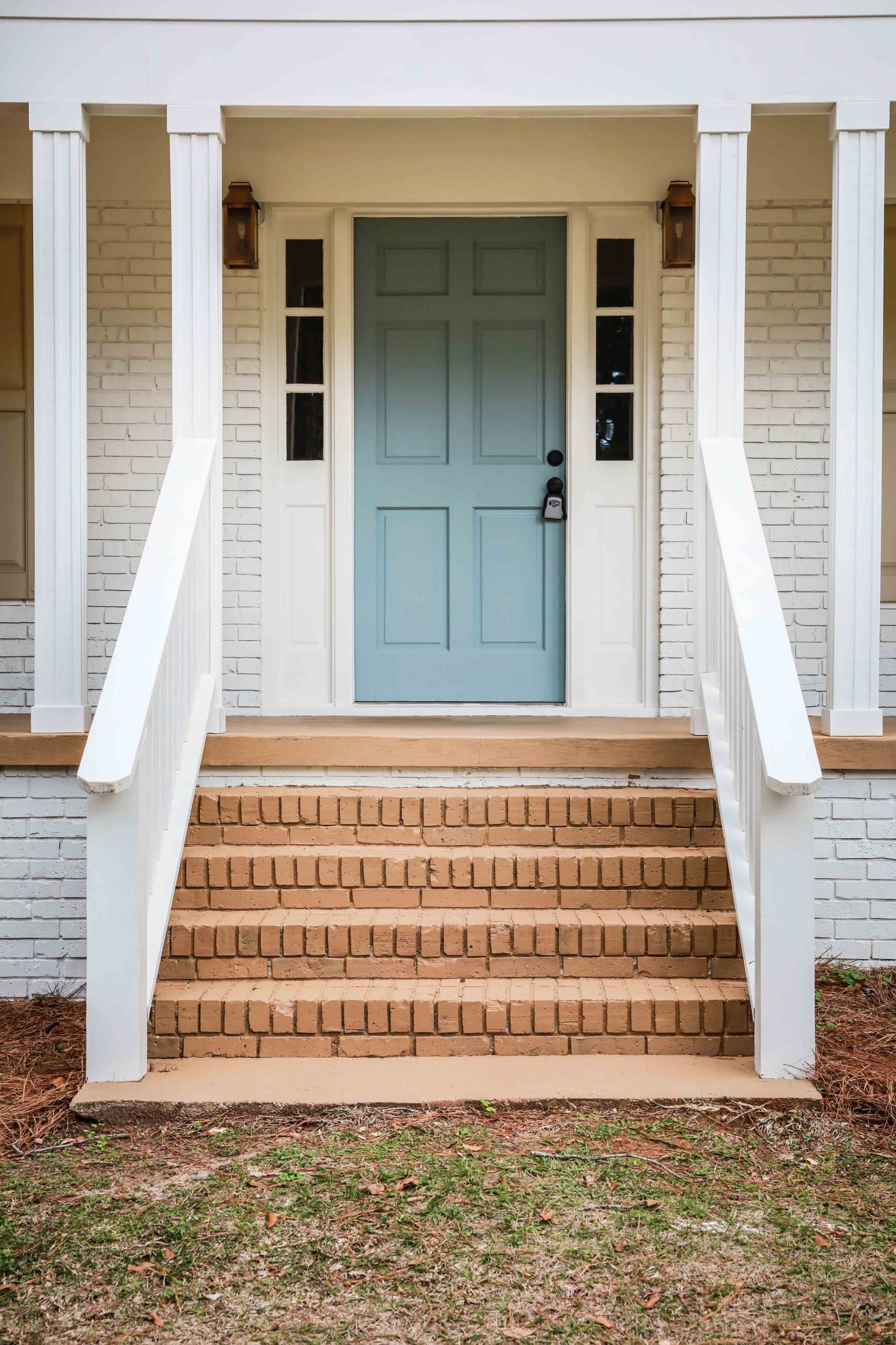 Front porch with brick steps, white railings, and a light blue front door on a white house. Front porch with brick steps, white railings, and a light blue front door on a white house.