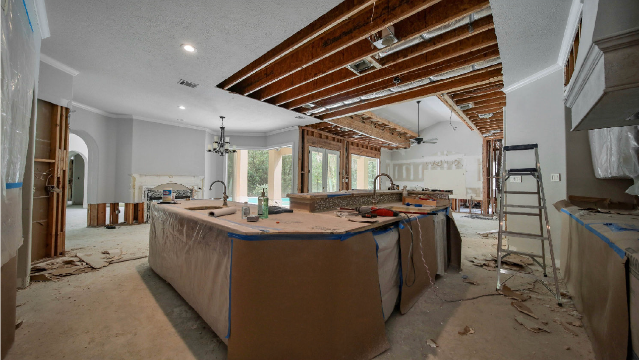 Renovated living room with exposed ceiling beams, large island, and construction materials scattered around