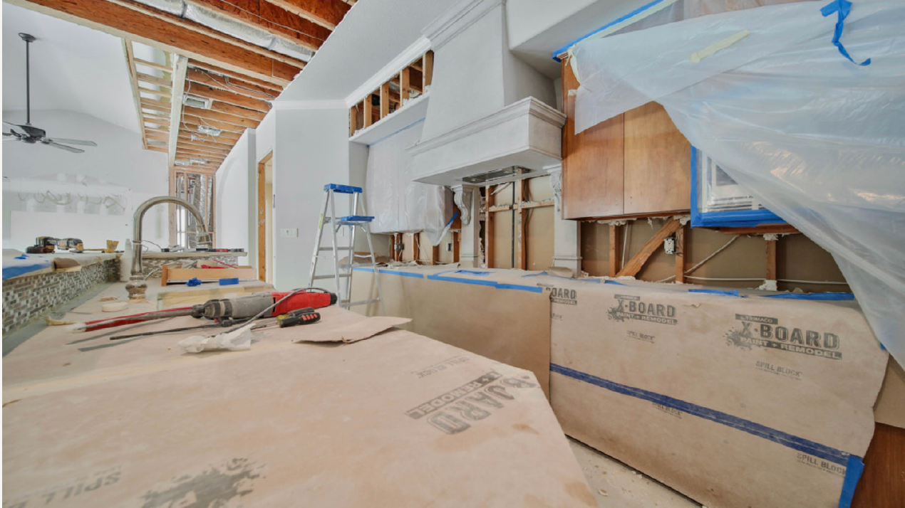 Renovation site with exposed beams, plastic-covered walls, tools, and construction materials scattered on the floor