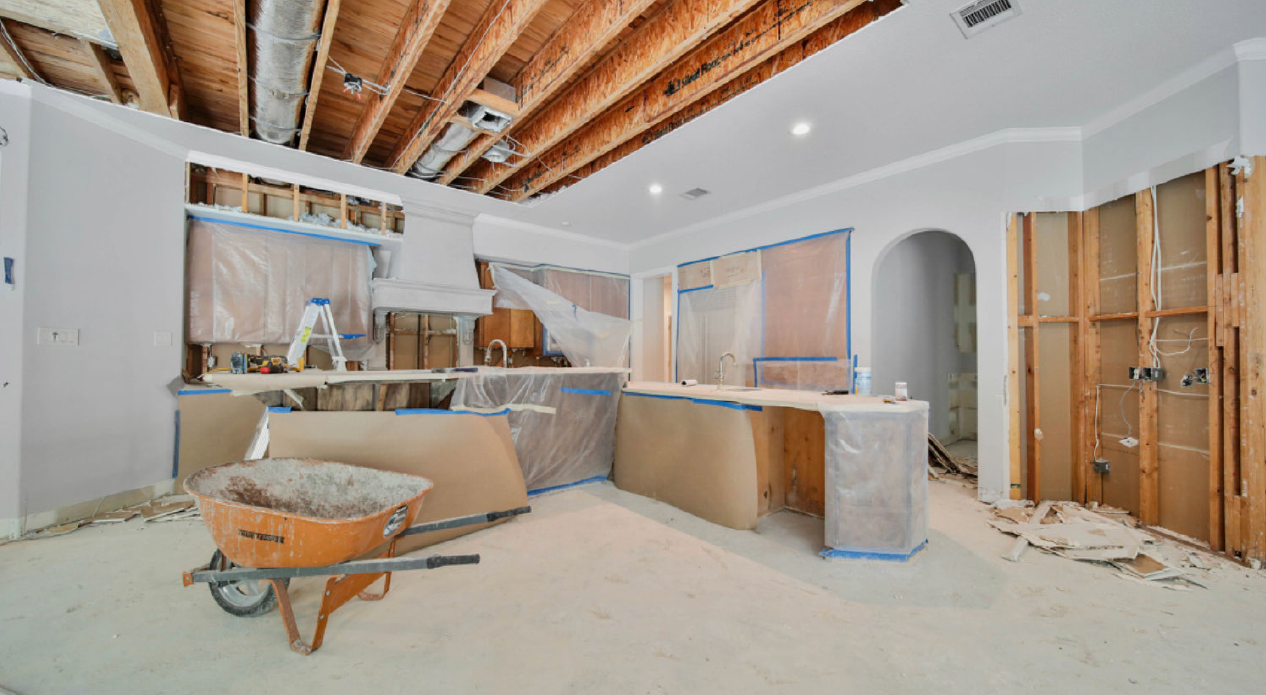 Kitchen under renovation with exposed ceiling beams, unfinished cabinets, and construction dust on the floor