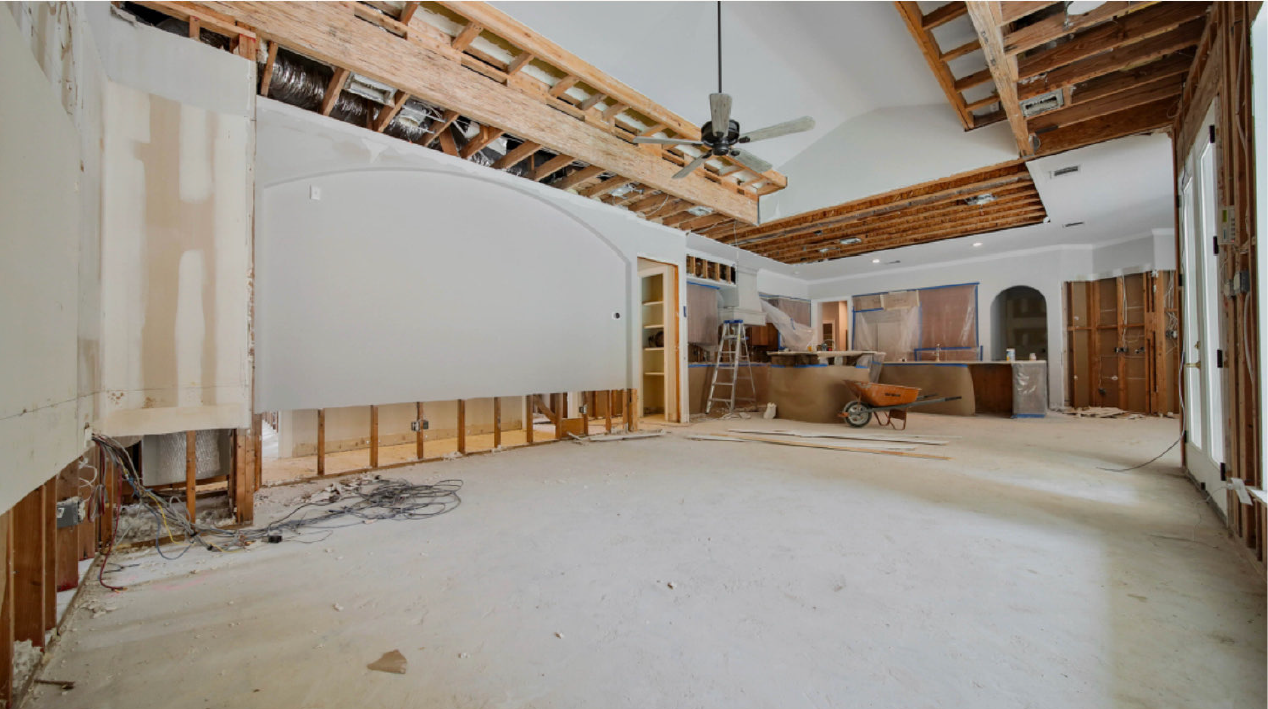 Partially renovated interior with exposed ceiling beams, drywall, and construction materials on the floor