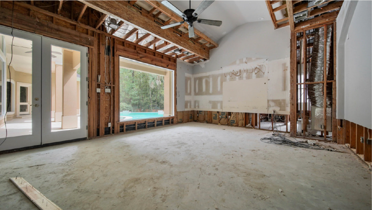 Interior of a room under renovation with exposed framing, unfinished ceiling, and large windows.
